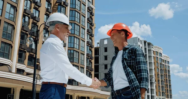 Ingeniero maduro y constructor estrechando las manos y hablando en el sitio de construcción — Stock Photo