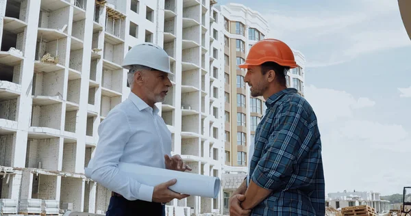 Вид збоку інженера з кресленнями розмовляючи з будівельником на будівельному майданчику — стокове фото