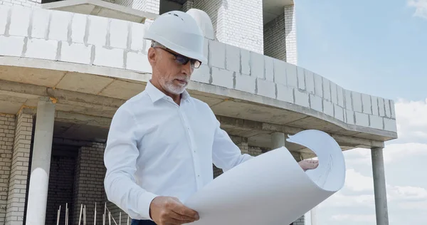Mature engineer with blueprint on construction site — Stock Photo