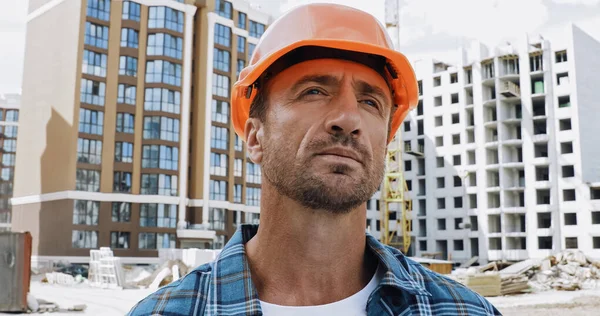 Constructor guapo mirando hacia otro lado en el sitio de construcción - foto de stock