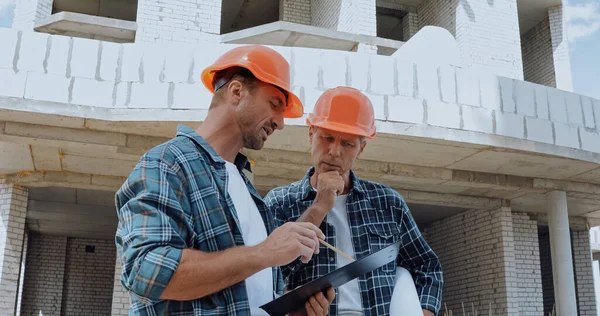 Constructores mirando el portapapeles y hablando en el sitio de construcción - foto de stock