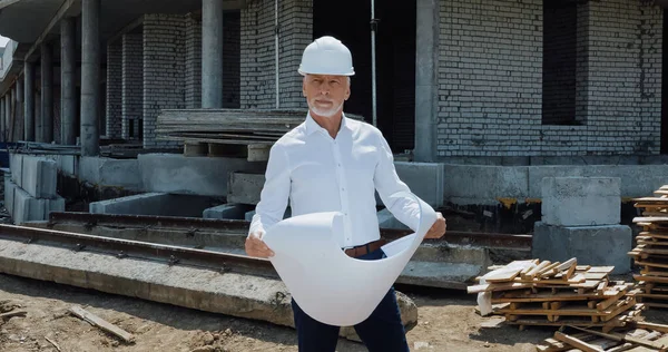 Reifer Ingenieur mit hartem Hut hält Bauplan auf Baustelle — Stockfoto