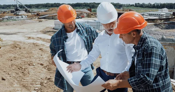 Ingegnere e costruttori parlando e guardando cianografia in cantiere — Foto stock