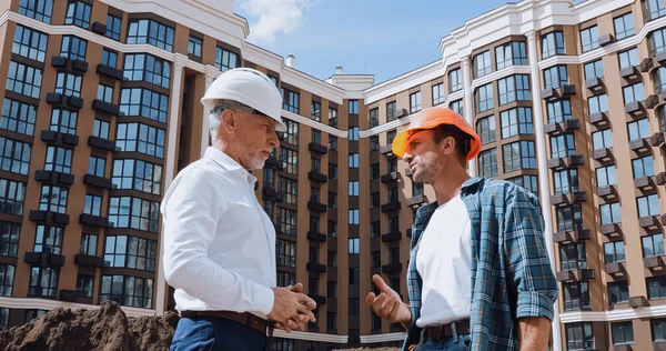 Low angle view of engineer and builder talking near new building — Stock Photo