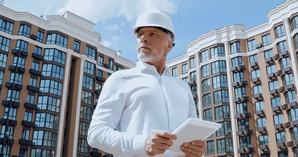 Niedrigwinkel-Ansicht eines reifen Ingenieurs mit digitalem Tablet mit Gebäude an der Stadtstraße im Hintergrund — Stockfoto