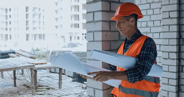 Constructor pensativo en casco mirando el plano en el sitio de construcción - foto de stock