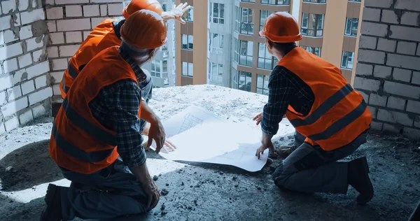 Builders in hand hats discussing blueprint while sitting on construction site — Stock Photo