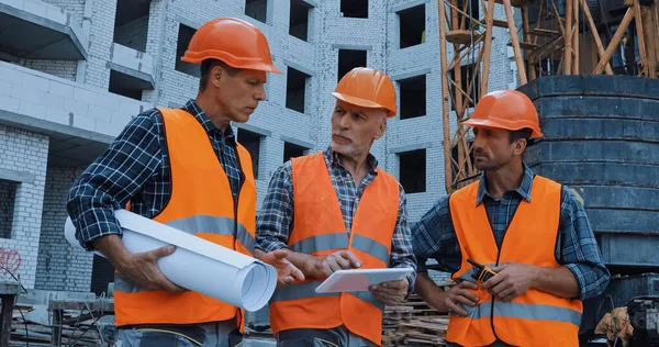 Builders with equipment talking near building crane on construction site — Stock Photo