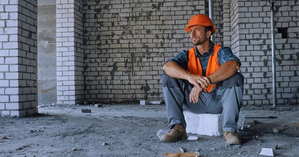 Constructor en chaleco de seguridad y casco mirando hacia otro lado en el sitio de construcción - foto de stock