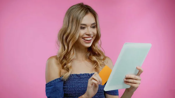 Весела жінка тримає кредитну картку і цифровий планшет ізольовано на рожевому — стокове фото