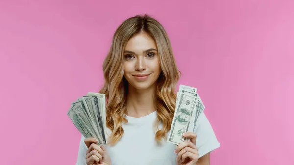 Весела молода жінка в білій футболці тримає долари ізольовано на рожевому — стокове фото