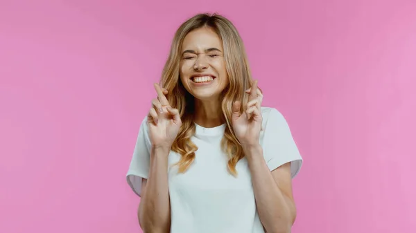 Blonde woman with crossed fingers and closed eyes isolated on pink — Stock Photo