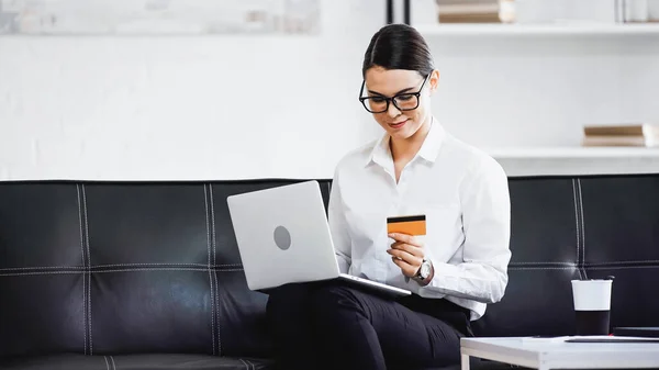 Молодая деловая женщина сидит на диване с ноутбуком и кредитной картой — стоковое фото