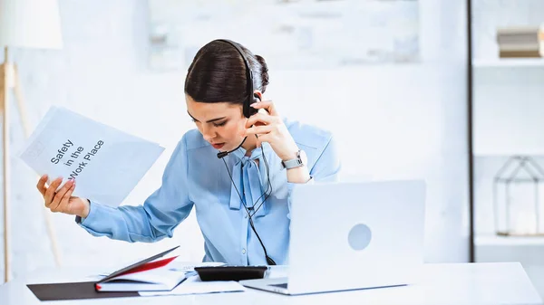 Giovane operatore di call center che tiene l'istruzione di sicurezza in posto di lavoro vicino a computer portatile in ufficio — Foto stock