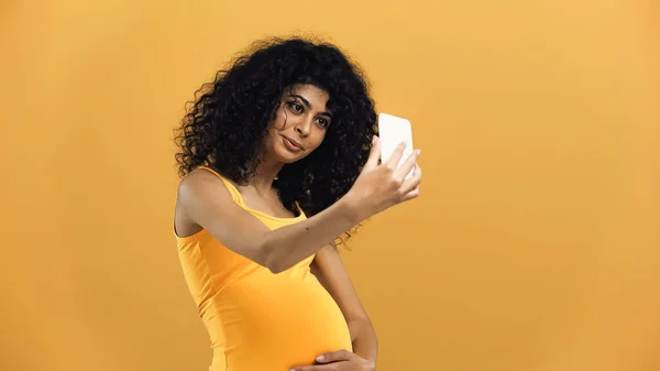 Pregnant hispanic woman taking selfie isolated on yellow — Stock Photo