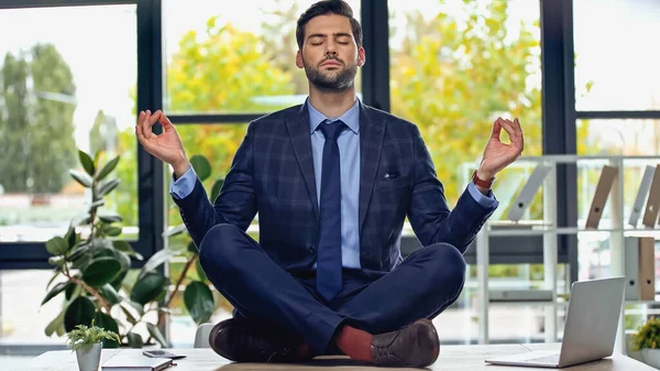 Hombre de negocios en traje meditando en escritorio en la oficina - foto de stock