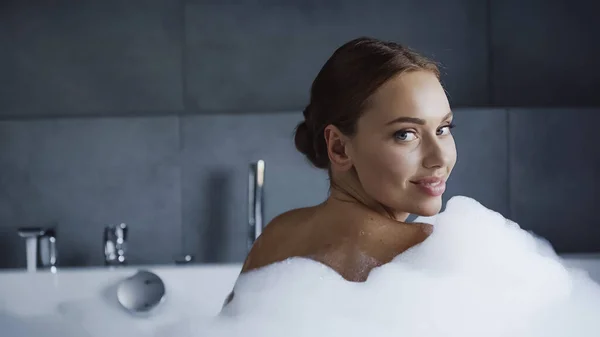 Donna sorridente che fa il bagno con schiuma nella vasca bianca — Foto stock