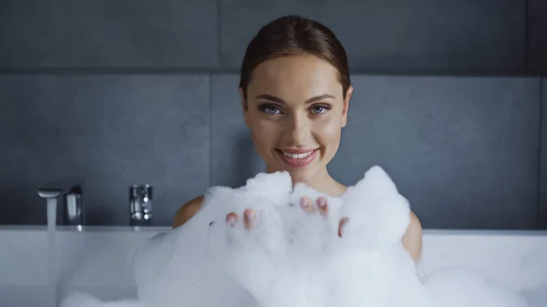 Sorridente giovane donna che fa il bagno con schiuma nella vasca da bagno bianca — Foto stock