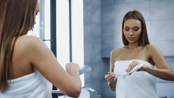 Jeune femme floue en serviette appliquer du dentifrice sur la brosse à dents — Photo de stock