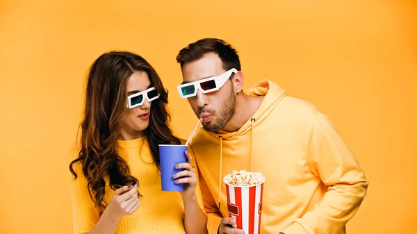 Hombre beber soda con paja cerca de novia en gafas 3d aislado en amarillo - foto de stock