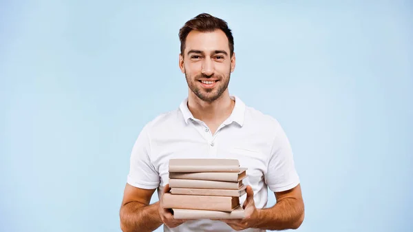 Alegre hombre sosteniendo pila de libros aislados en azul - foto de stock