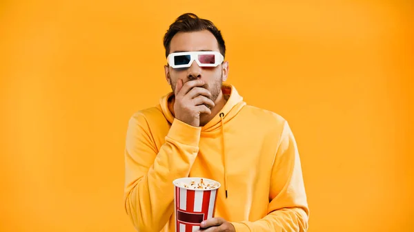 Homem em óculos 3d segurando balde de pipoca e cobrindo boca isolada em amarelo — Fotografia de Stock