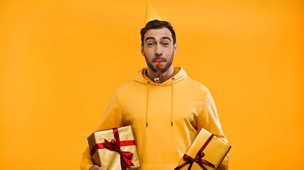 Man blowing in party horn and holding presents isolated on yellow — Stock Photo