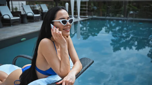 Happy woman in sunglasses lying on sunbed and talking on smartphone — Stock Photo