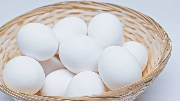 Plenty of chicken eggs in wicker basket on white surface — Stock Photo