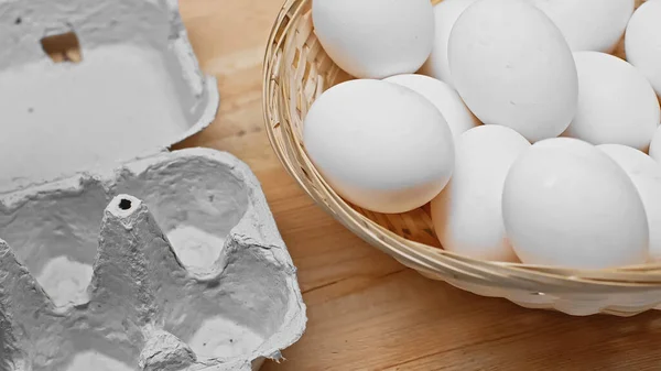 Eierschale und Weidenkorb mit vielen weißen Eiern auf Holztisch — Stockfoto