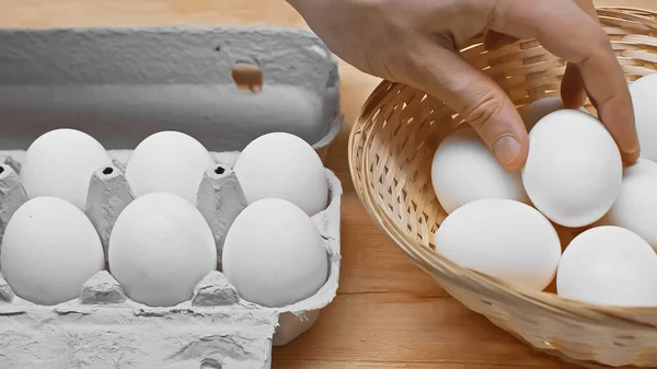 Abgeschnittene Ansicht eines Mannes, der Ei aus Weidenkorb in der Nähe von Eierschale auf Holztisch nimmt — Stockfoto