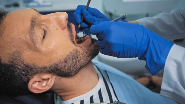 Dentista examinando dentes de homem com espelho bucal e sonda dentária — Fotografia de Stock