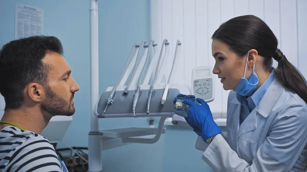Estomatólogo apuntando al modelo de dientes cerca del paciente en la clínica dental - foto de stock