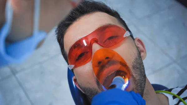 Zahnarzt mit UV-Lampe in der Nähe des Patienten mit Brille, verschwommener Vordergrund — Stockfoto