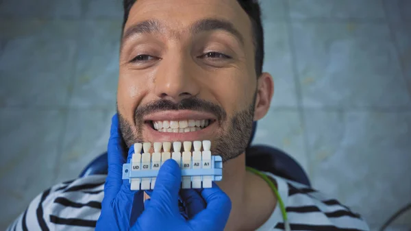 Overhead view of smiling man near dentist holding teeth color palette — Stock Photo