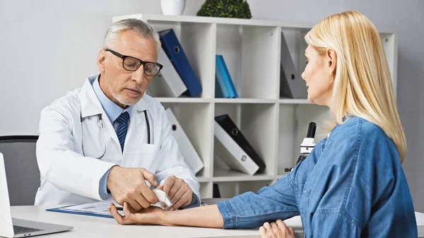 Doctor en gafas graduadas midiendo temperatura de mujer rubia con pirómetro - foto de stock