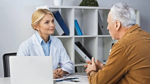 Зрілий чоловік розмовляє зі усміхненим лікарем під час консультації в клініці — стокове фото