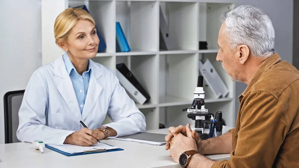 Médecin souriant tenant le stylo tout en écoutant le patient pendant la consultation — Photo de stock