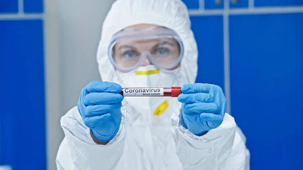 Virologe im Warnanzug zeigt Reagenzglas mit Coronavirus-Schriftzug im Labor — Stockfoto