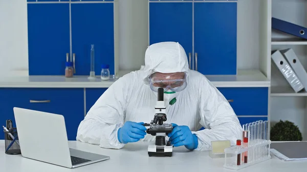 Cientista trabalhando com microscópio perto de laptop em laboratório — Fotografia de Stock