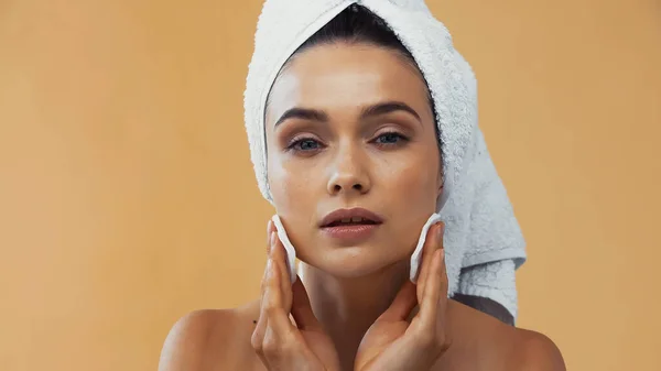 Giovane donna con asciugamano sulla testa pulizia viso con batuffoli di cotone isolato su beige — Foto stock