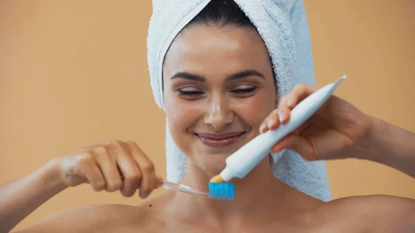 Femme souriante avec serviette sur la tête appliquer du dentifrice sur une brosse à dents isolée sur beige — Photo de stock