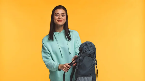 Viajero sonriente sosteniendo la mochila y mirando a la cámara aislada en amarillo - foto de stock