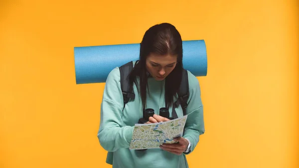 Young tourist with backpack looking at map isolated on yellow — Stock Photo