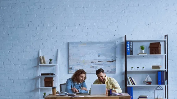 Joyeux hommes d'affaires travaillant près d'un ordinateur portable dans un bureau moderne — Photo de stock