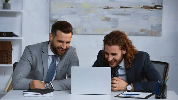 Partner commerciali eccitati ridendo vicino al laptop in ufficio — Foto stock