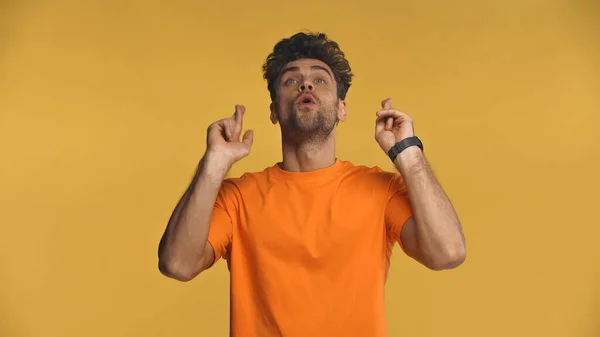 Man with crossed fingers looking up isolated on yellow — Stock Photo