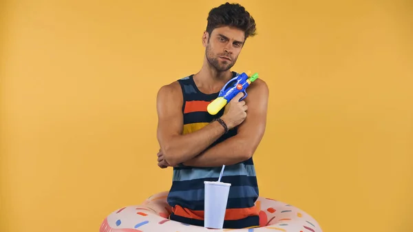 Man in inflatable ring holding water gun isolated on yellow — Stock Photo