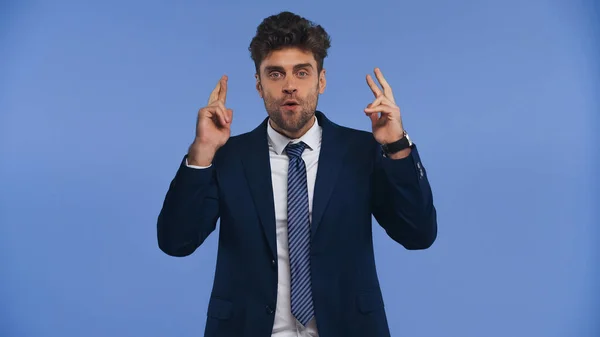 Amazed businessman with crossed fingers looking at camera isolated on blue — Stock Photo