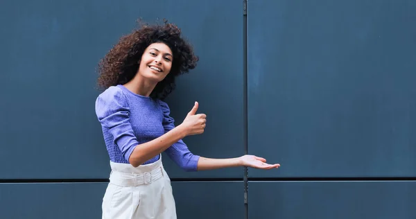 Cheerful young woman pointing with hand and showing thumb up outside — Stock Photo